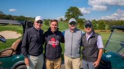 Four men standing in front of golf cart on golf course