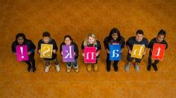 Students looking up at the camera and holding up signs that spell out, thanks!