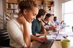 A young woman smiles looking at a laptop.