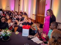 A professor hugs a student seated at a table after presenting her with an award.