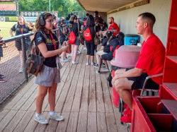 A student interviews a baseball player in a dugout.