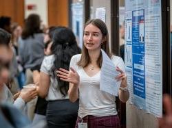 A student gestures as she discusses her research poster.