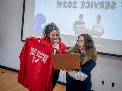 Student 马里亚纳Luna-马丁内斯 holds a computer as Bonner Leader and Service Coordinator Mikaela Guzman looks on while holding a Montclair sweatshirt.