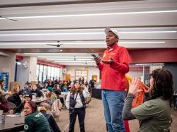 Richard Steiner-Otoo stands on a chair while addressing a roomful of fellow volunteers.