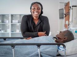 Elsie Alabi-Gonzalez, Clinical Specialist, standing in the School of Nursing's Simulation Center in front of a medical manikin.