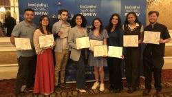 Eight standing and smiling students in front of a branded backdrop. each holding certificates of recognition from the FOLIO Awards.