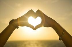 Two women making a heart with their hands in front of the sunset.