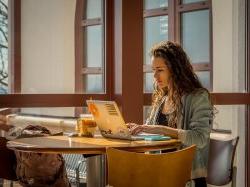 Photo of student working on laptop at table in campus building.