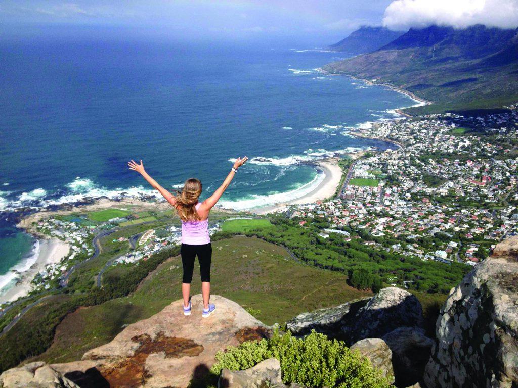 Girl with hands raised standing on a cliff overlooking the ocean